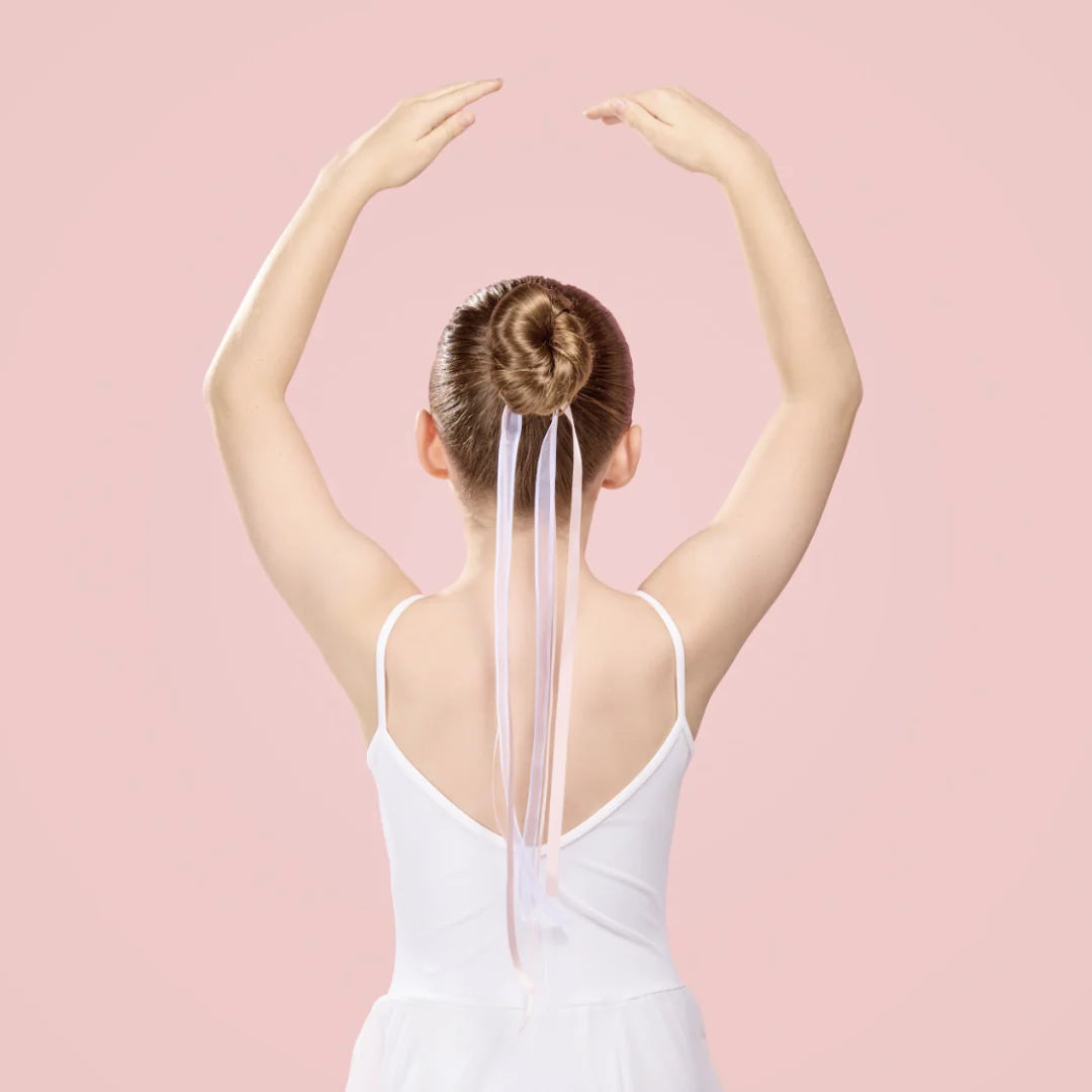 Ballerina with a long hair ribbon in a bun against a pink background