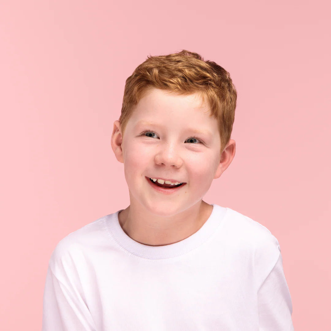 Young boy with red hair smiling against a pink background